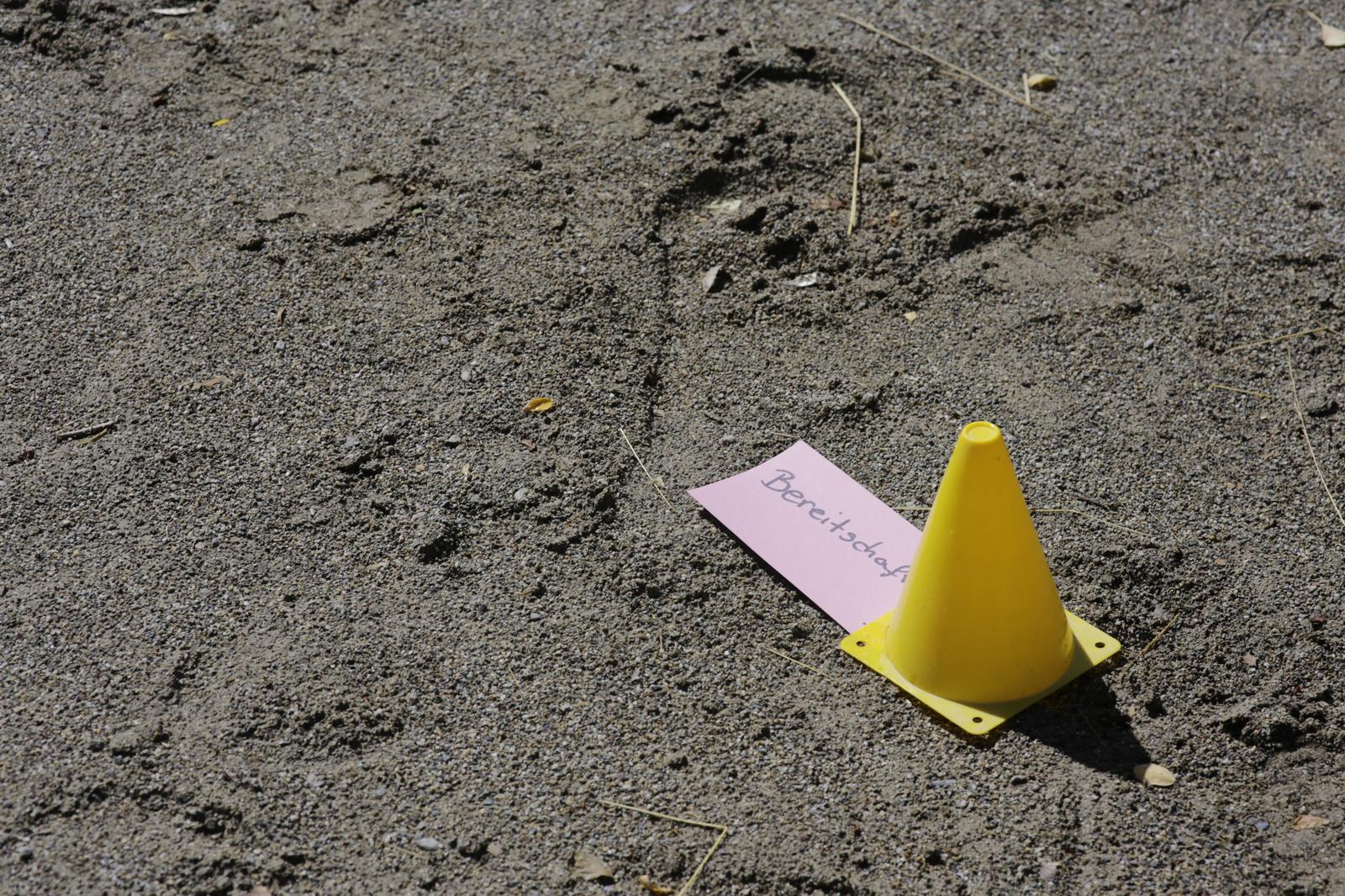 Eine Karte mit der Aufschrift Bereitschaft liegt neben einem Markierungshütchen im Sand.